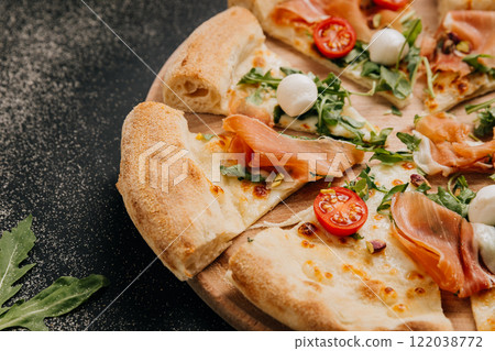 Delicious prosciutto and arugula pizza with cherry tomatoes and mozzarella on a wooden platter Delicious prosciutto and arugula pizza with cherry tomatoes and mozzarella on a wooden platter 122038772