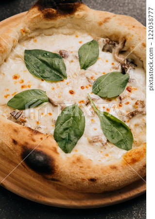 Delicious white pizza with creamy mushrooms, melted cheese, and fresh spinach leaves on wooden plate 122038777