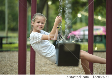 Young pretty happy smiling teenage small girl having fun on playground swings on summer vacations sunny day 122039232