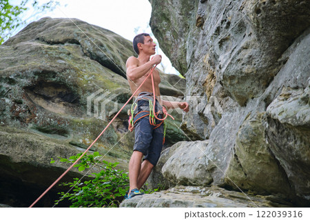 Strong male climber climbing steep wall of rocky mountain. Sportsman overcoming difficult route. Engaging in extreme sports hobby concept. 122039316