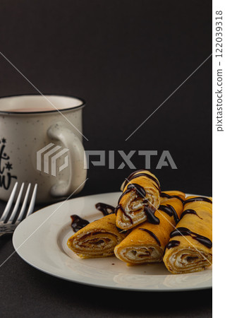 Delicious rolled pancakes with chocolate sauce and coffee on a table Delicious rolled pancakes with chocolate sauce and coffee on a table 122039318