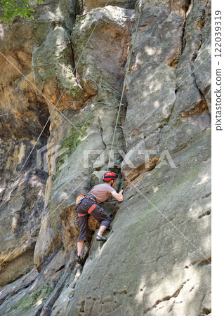 Strong male climber climbing steep wall of rocky mountain. Sportsman overcoming difficult route. Engaging in extreme sports hobby concept. 122039319