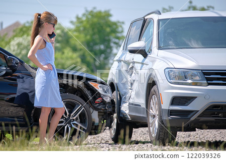 Stressed driver talking on sellphone on roadside near her smashed vehicle calling for emergency service help after car accident. Road safety and insurance concept Stressed driver talking on sellphone on roadside near her smashed vehicle calling for emergency service help after car accident. Road safety and insurance concept 122039326