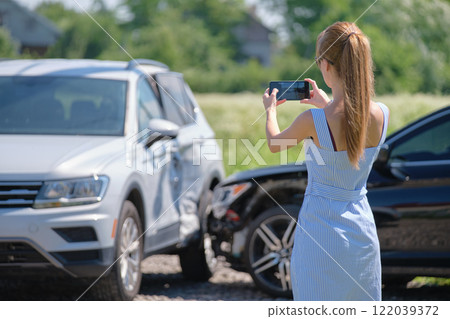 Sad female driver photographing on sellphone camera wrecked vehicles on street side for insurance service after car accident. Road safety concept 122039372