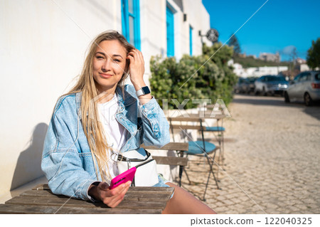 Smiling woman holding smartphone while sitting at 122040325