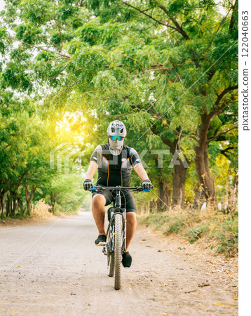 Professional cyclist on a dirt road. Fat cyclist on a dirt road surrounded by trees, Lifestyle of a chubby cyclist on the road Professional cyclist on a dirt road. Fat cyclist on a dirt road surrounded by trees, Lifestyle of a chubby cyclist on the road 122040663