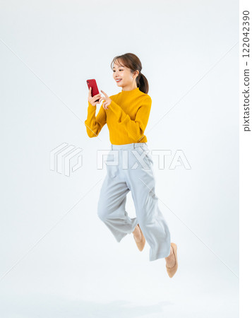 Full-body photo of a woman jumping while looking at her smartphone 122042390