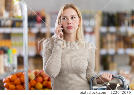 Upset girl talking on smartphone while shopping in supermarket Upset girl talking on smartphone while shopping in supermarket 122042679