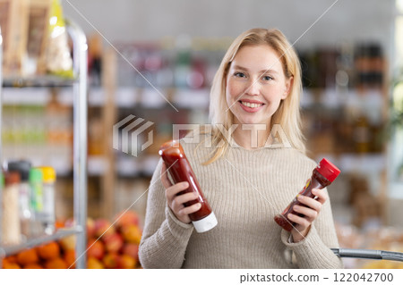 Girl shopping at supermarket - choosing ketchup in grocery supermarket 122042700