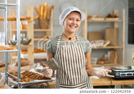 Young baker girl is standing near work table in kitchen, working with dough 122042856