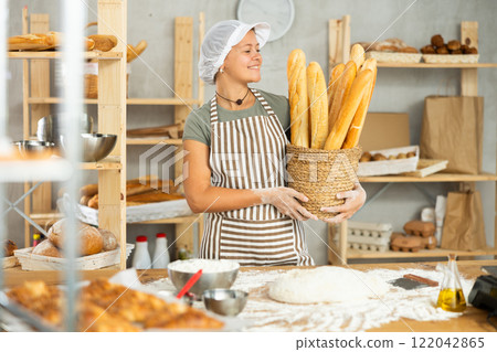 Young woman baker are standing near product range in bakery kitchen. Young woman baker are standing near product range in bakery kitchen. 122042865