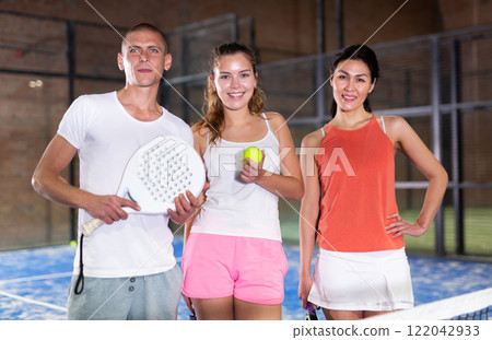 Three smiling players man and two women with padel rackets Three smiling players man and two women with padel rackets 122042933