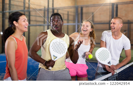 Four smiling men and women with padel rackets posing at court 122042954