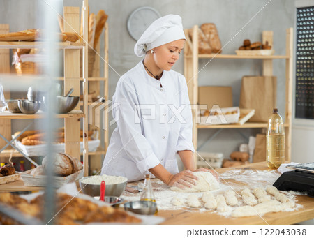 Woman works in bakery as baker, kneads dough, works with flour. 122043038