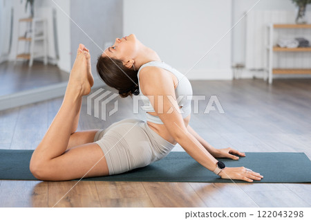 Young female yoga practitioner performing Raja Bhujangasana Young female yoga practitioner performing Raja Bhujangasana 122043298