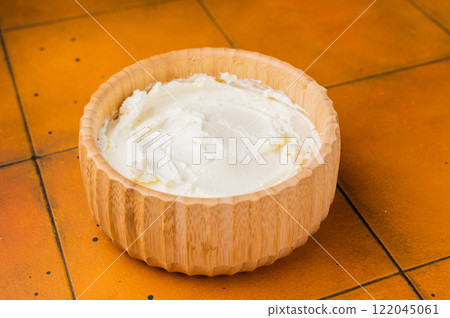 Cream texture, Mascarpone Italian cream cheese in wooden bowl. orange background. top view Cream texture, Mascarpone Italian cream cheese in wooden bowl. orange background. top view 122045061