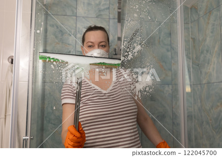 A woman is diligently cleaning the shower with a squeegee in a beautifully modern bathroom 122045700