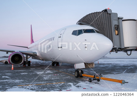 Jet plane with towbar near the boarding bridge at winter airport apron 122046364