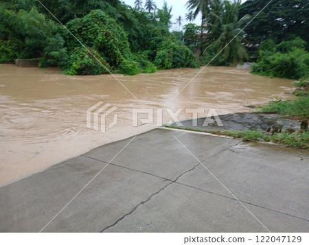Brown water flood flowing and flooding concrete road until cars can't travel 122047129