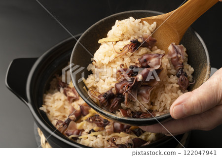 將用砂鍋煮熟的螢火蟲魷魚飯盛入碗中。 將用砂鍋煮熟的螢火蟲魷魚飯盛入碗中。 122047941