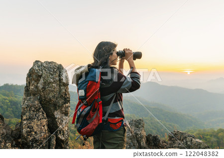 woman is standing on a mountain top, looking through a binoculars woman is standing on a mountain top, looking through a binoculars 122048382