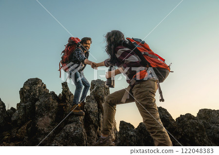 man and a woman are helping each other climb a mountain man and a woman are helping each other climb a mountain 122048383