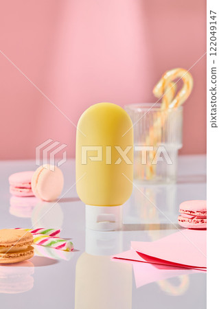 A pale yellow squeeze bottle mockup, surrounded by pastel pink macarons, candy canes, and folded pink card stock, forms the centerpiece of a dessert table concept against a solid pink backdrop. A pale yellow squeeze bottle mockup, surrounded by pastel pink macarons, candy canes, and folded pink card stock, forms the centerpiece of a dessert table concept against a solid pink backdrop. 122049147