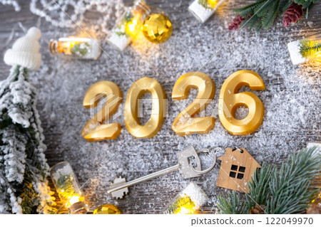 New Year 2026 golden numbers and House key with tiny form of home on festive grey wooden background flatlay, lights of garlands, greeting card. Housing, real estate, relocation, mortgage, insurance 122049970