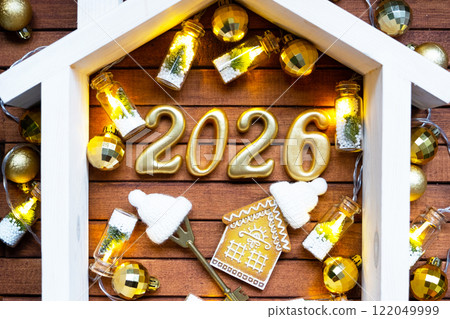 Golden figures number 2026 and tiny home on background of cozy windows of a house with warm light with festive decor of stars,snow and garlands. Greeting card, Happy New Year, cozy home 122049999