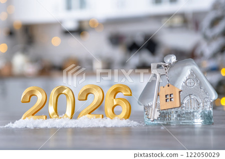 Golden number 2026, key and tiny home on background of cozy white kitchen with Christmas tree and Christmas decor with garland lights. Housing, interior, renovation, mortgage, rent in New Year 122050029