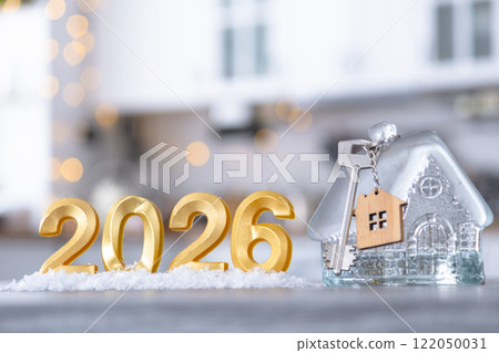 Golden number 2026, key and tiny home on background of cozy white kitchen with Christmas tree and Christmas decor with garland lights. Housing, interior, renovation, mortgage, rent in New Year 122050031