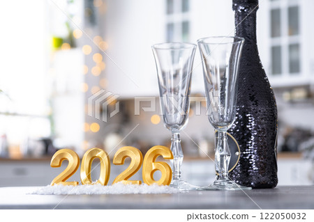 Golden number 2026 with bottle of sparkling wine and glasses on table of cozy white kitchen with Christmas tree and garland lights. Housing, interior, renovation, mortgage, rent in New Year 122050032