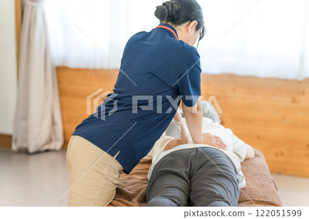 A female massage therapist and physical therapist massaging a senior woman 122051599