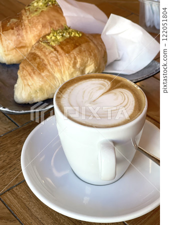 Cappuccino in cup on saucer on table. Croissant with pistachio cream. Food and drinks. Cappuccino in cup on saucer on table. Croissant with pistachio cream. Food and drinks. 122051804