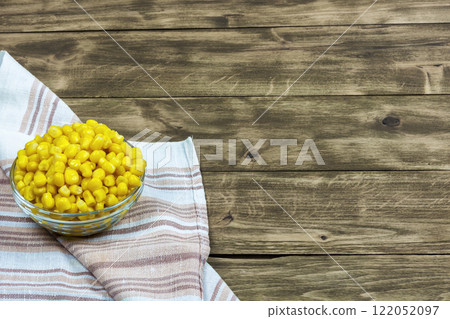 Glass salad bowl with grains of corn is on a napkin on a wooden surface Glass salad bowl with grains of corn is on a napkin on a wooden surface 122052097