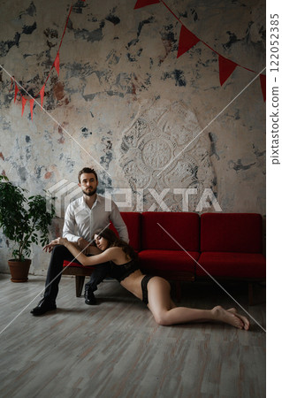 A girl in underwear lies at the feet of a guy in a business suit against the backdrop of a loft interior 122052385