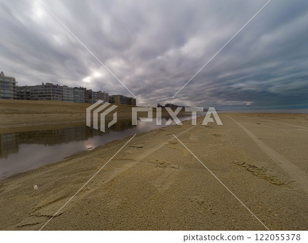 Dramatic Beach Scene with Reflections and Residential Buildings under Overcast Sky Dramatic Beach Scene with Reflections and Residential Buildings under Overcast Sky 122055378