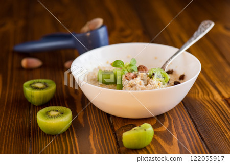 cooked oatmeal with kiwi, honey and nuts in a bowl on a wooden table cooked oatmeal with kiwi, honey and nuts in a bowl on a wooden table 122055917