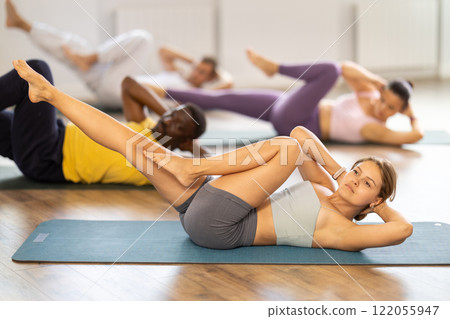 Female pilates instructor performing bicycle crunches with group Female pilates instructor performing bicycle crunches with group 122055947