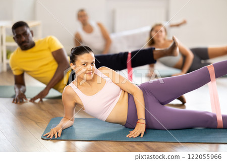 Asian woman exercising with loop band during group pilates class Asian woman exercising with loop band during group pilates class 122055966