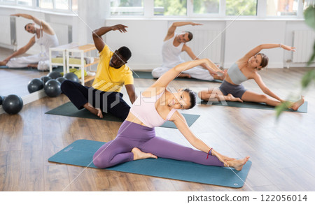 Young Asian teacher working out Parivritta Janu Shirshasana with multinational students group 122056014