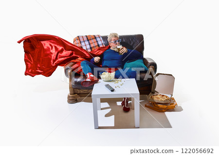 Man in superhero costume and 3D glasses sitting on couch, eating popcorn and sipping beer, open pizza boxes on floor against white background 122056692
