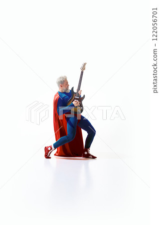 Dynamic image of grey-haired man in superhero costume with red cape emotionally playing electric guitar against swift studio background 122056701