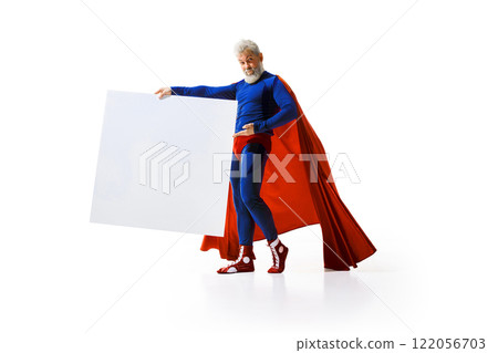Grey-haired man in superhero costume standing in pose of bullfighter with big white poster with empty space against white studio background 122056703