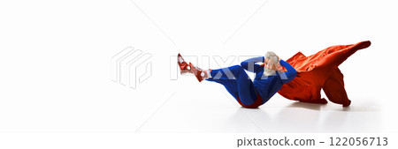 Grey-haired young man with beard, in superhero costume and reed cape, doing bicycle crunches, press exercises against white studio background Grey-haired young man with beard, in superhero costume and reed cape, doing bicycle crunches, press exercises against white studio background 122056713
