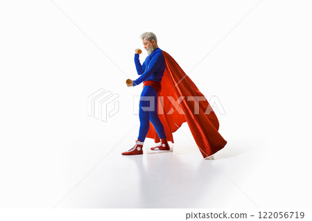 Grey-haired man in superhero costume with red cape training with dumbbells, against white studio background 122056719