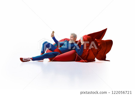 Grey-haired man in superhero costume lounging on red beanbag, holding glass of milk and cookie with a playful face Grey-haired man in superhero costume lounging on red beanbag, holding glass of milk and cookie with a playful face 122056721