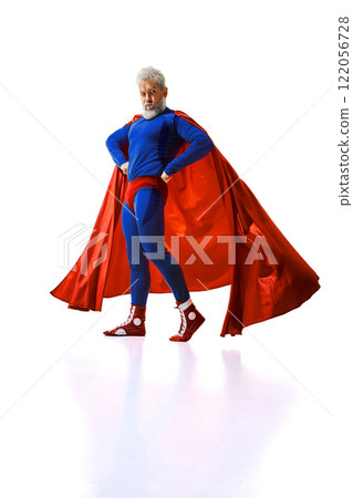Funny man with grey hair and beard standing in blue superhero suit with red cape, executing joy against white studio background. 122056728