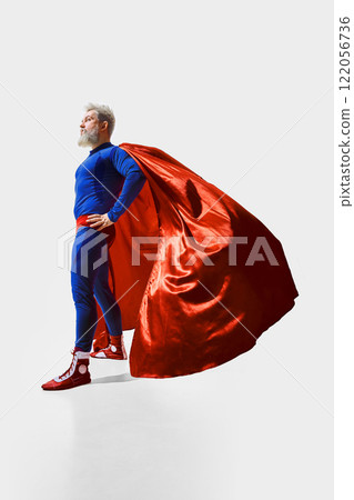 Full-length slightly low-angle view of a bearded man in image of a superhero wearing blue costume with red cape 122056736