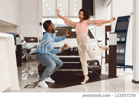 New Car Owners. Joyful African Couple Jumping Celebrating Buying Automobile In Dealership Showroom 122057230